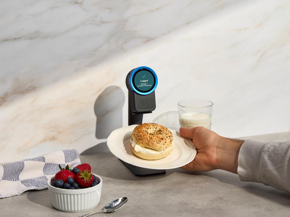 A bagel with cream cheese held up to the Trepo device on its countertop stand, which reads Logged - bagel + cream cheese