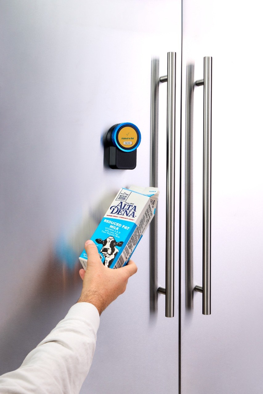An empty milk carton held up to the Trepo device, which takes it out of the kitchen and adds it to the shopping list