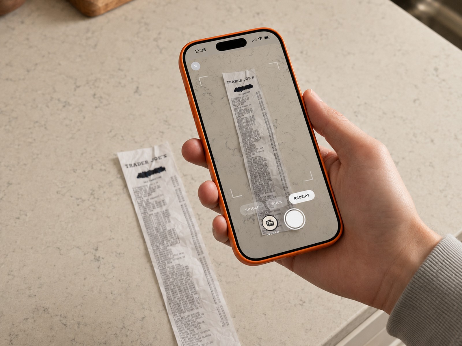 A hand holding a phone over a kitchen worktop, photographing a Trader Joe's receipt inside the Trepo capture frame