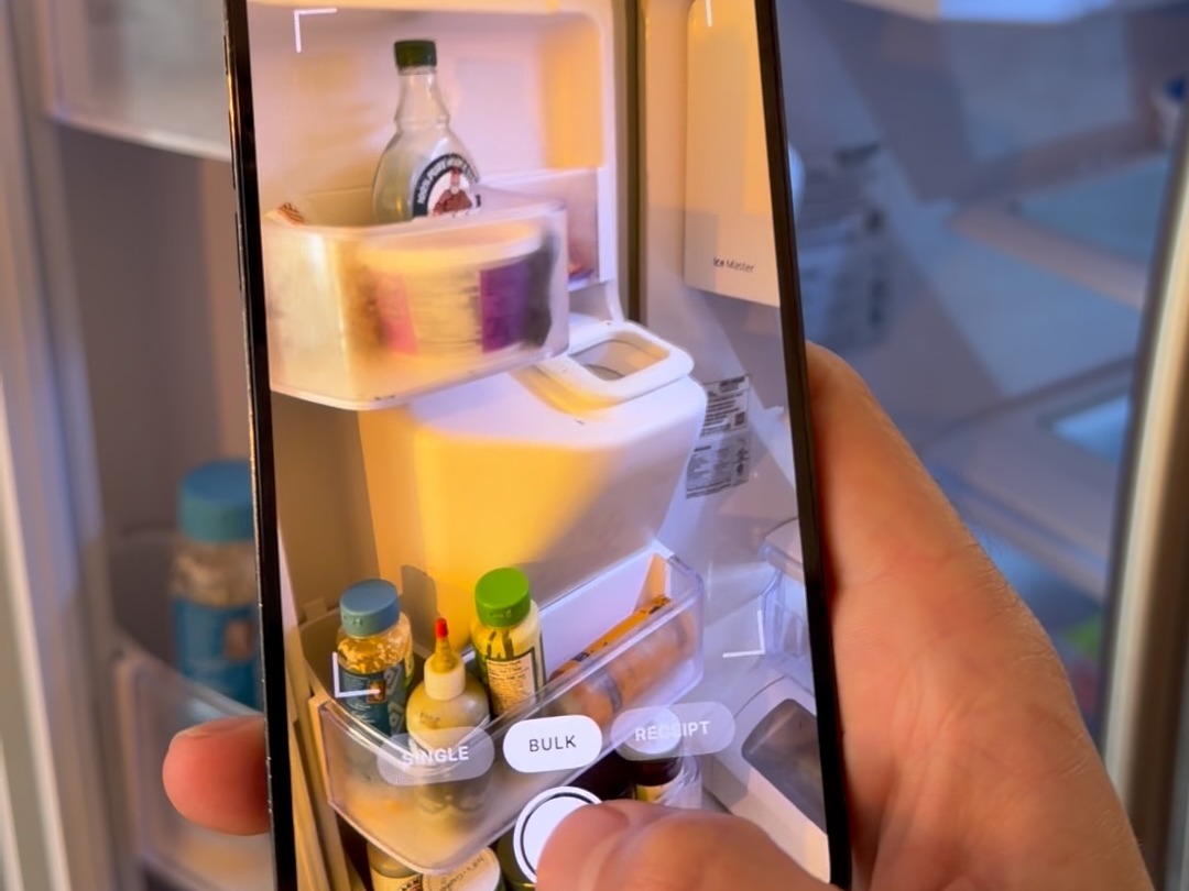 A phone held up to an open fridge, the Trepo camera framing the shelves to identify what's inside