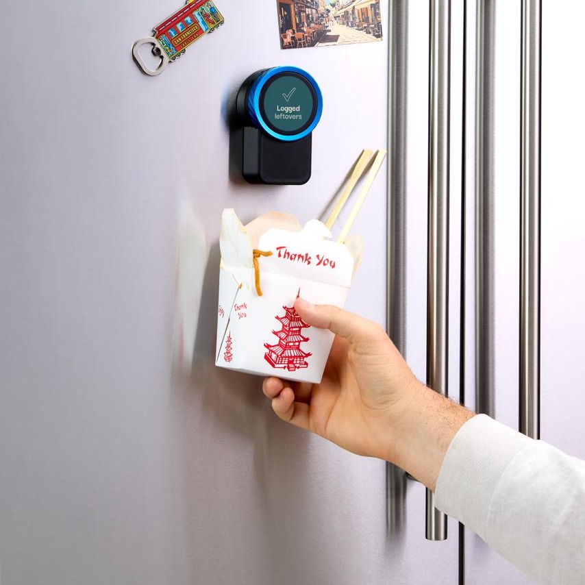 A takeout box held up to the Trepo device on the fridge door, which reads Logged — leftovers